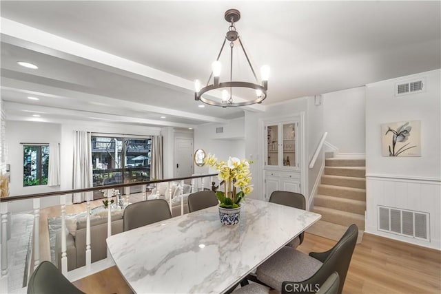 dining space with beam ceiling, visible vents, light wood finished floors, and stairs