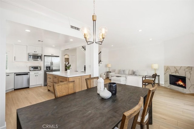 dining space with light wood-style floors, visible vents, a fireplace, and an inviting chandelier