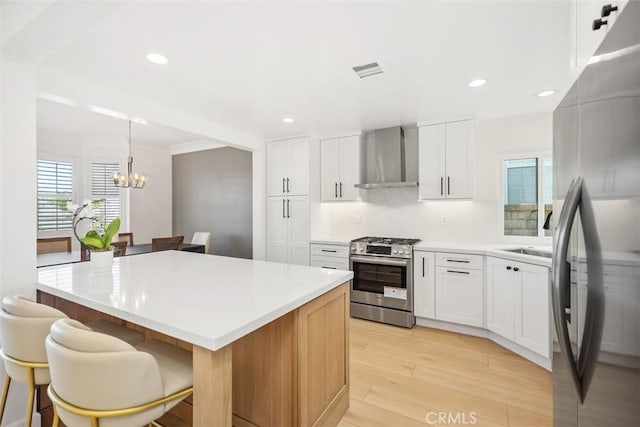 kitchen featuring light wood-style flooring, a breakfast bar area, stainless steel appliances, wall chimney range hood, and a sink