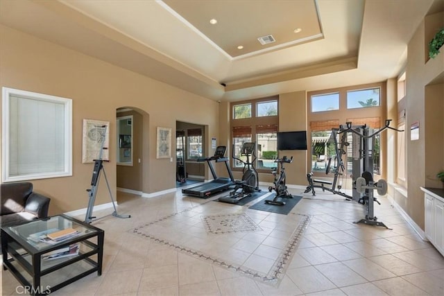 workout room with light tile patterned floors, baseboards, arched walkways, and a raised ceiling