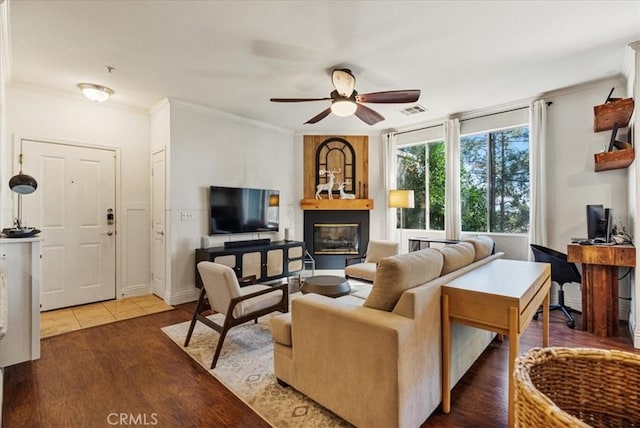 living area with ceiling fan, a fireplace, wood finished floors, visible vents, and crown molding