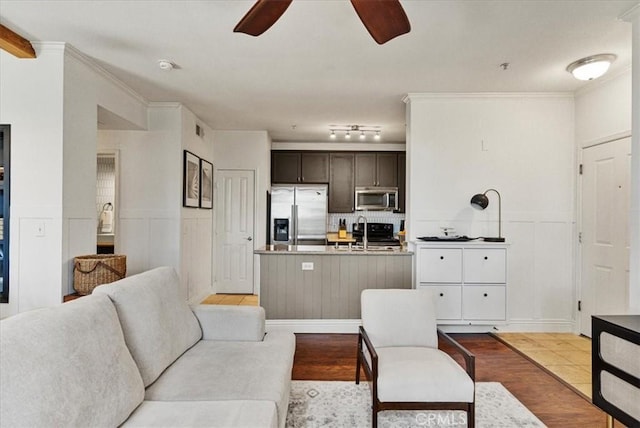 living room featuring wainscoting, light wood-type flooring, a ceiling fan, and crown molding