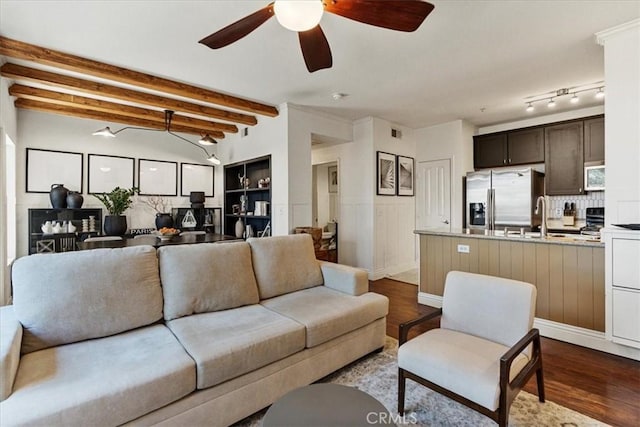 living room with ceiling fan, a wainscoted wall, wood finished floors, visible vents, and beam ceiling