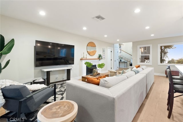 living area with a fireplace, recessed lighting, visible vents, light wood-style flooring, and stairway