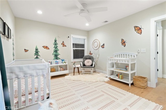 bedroom featuring a nursery area, light wood finished floors, recessed lighting, and baseboards