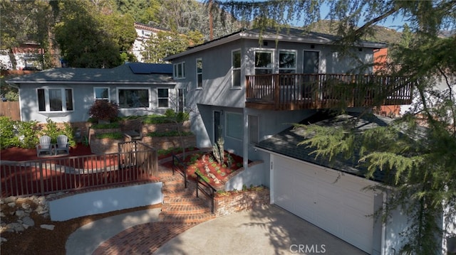 view of front of house featuring a garage, roof mounted solar panels, a deck, and stucco siding