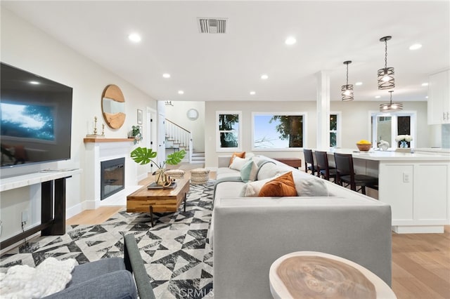 living area featuring visible vents, a glass covered fireplace, light wood-style flooring, and recessed lighting