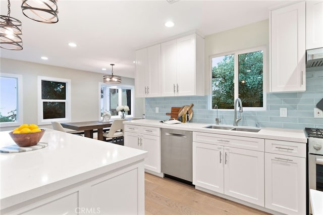 kitchen with appliances with stainless steel finishes, light countertops, white cabinetry, pendant lighting, and a sink