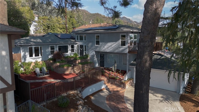 back of property featuring stucco siding, concrete driveway, roof mounted solar panels, a mountain view, and a garage