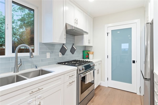 kitchen with under cabinet range hood, stainless steel appliances, a sink, white cabinets, and light countertops