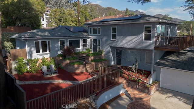 back of property featuring stucco siding, solar panels, an attached garage, a mountain view, and a balcony