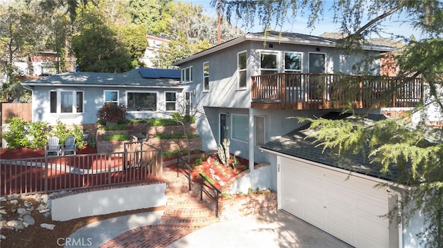 view of front of property featuring a garage, stucco siding, roof mounted solar panels, and a wooden deck