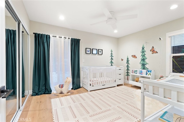 bedroom featuring a nursery area, recessed lighting, a closet, ceiling fan, and light wood-type flooring