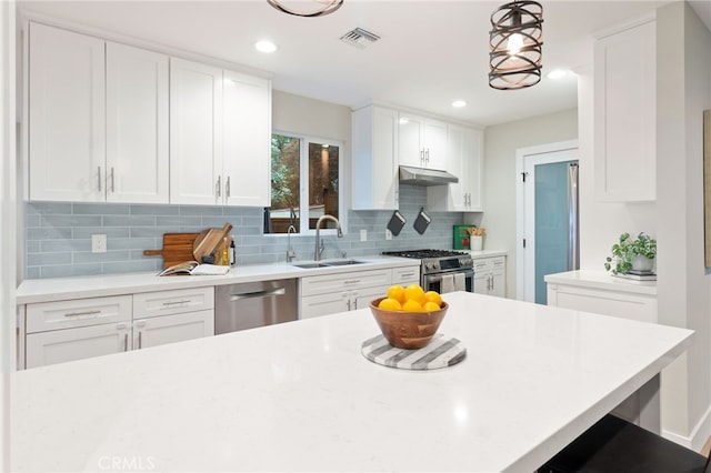 kitchen featuring white cabinets, decorative light fixtures, stainless steel appliances, light countertops, and a sink