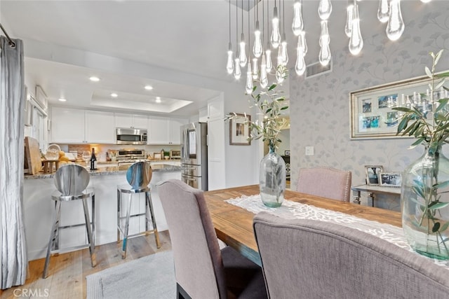 dining room with light wood-style floors, recessed lighting, a raised ceiling, and wallpapered walls