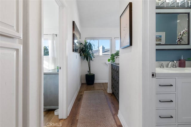 hall with light wood-style floors, a sink, and baseboards