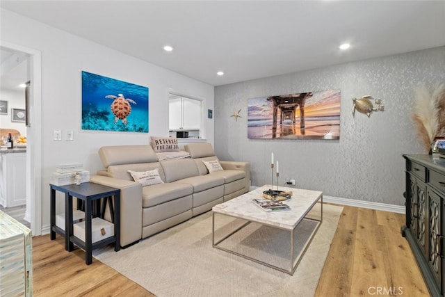 living area featuring recessed lighting, a textured wall, light wood-style flooring, and baseboards