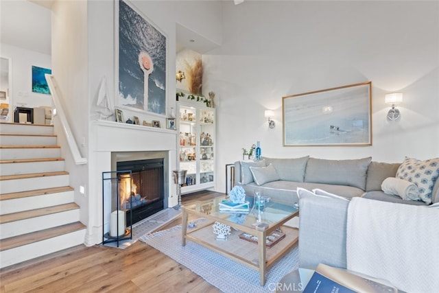 living room with a warm lit fireplace, a high ceiling, stairway, and wood finished floors