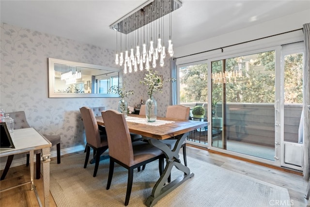 dining room featuring baseboards, an inviting chandelier, wood finished floors, and wallpapered walls