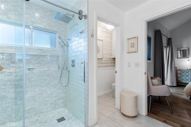 ensuite bathroom featuring toilet, a wainscoted wall, wood finished floors, a stall shower, and ensuite bath