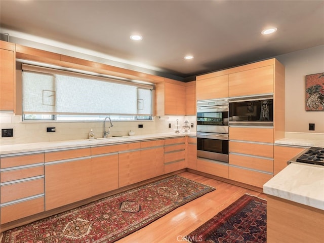 kitchen featuring light wood-style flooring, stainless steel appliances, a sink, light countertops, and light brown cabinetry