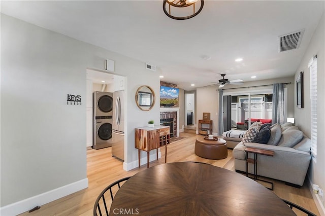 living area with a brick fireplace, stacked washing maching and dryer, visible vents, and light wood-style floors