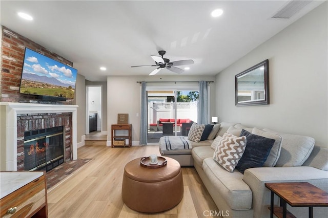 living room featuring baseboards, visible vents, light wood-style flooring, a fireplace, and recessed lighting