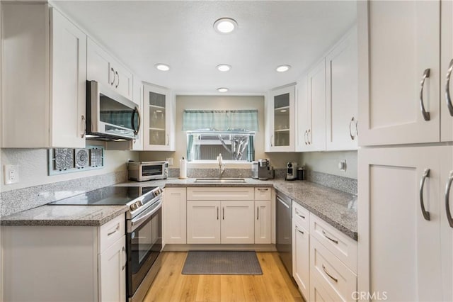 kitchen featuring stainless steel appliances, light wood-style flooring, glass insert cabinets, white cabinets, and a sink