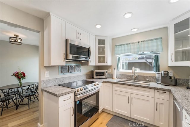 kitchen with appliances with stainless steel finishes, white cabinetry, a sink, and light wood finished floors