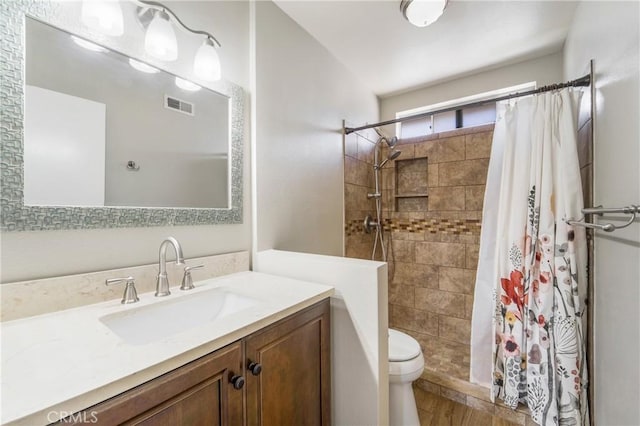 full bathroom featuring toilet, visible vents, tiled shower, and vanity