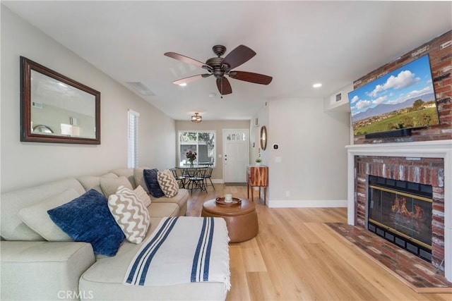 living area with wood finished floors, a ceiling fan, visible vents, baseboards, and a brick fireplace