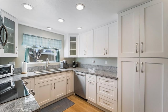 kitchen featuring white cabinets, dishwasher, light stone counters, light wood-style floors, and a sink