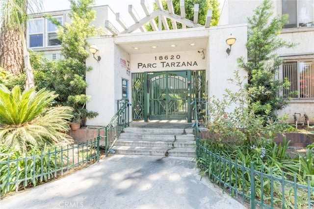 view of exterior entry featuring a gate, fence, and stucco siding