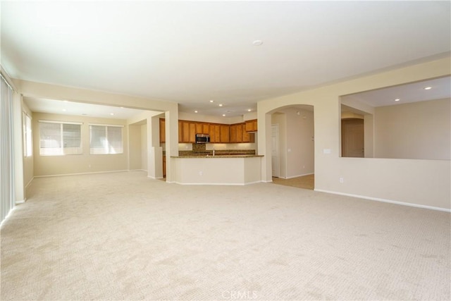 unfurnished living room with light carpet, baseboards, arched walkways, and recessed lighting