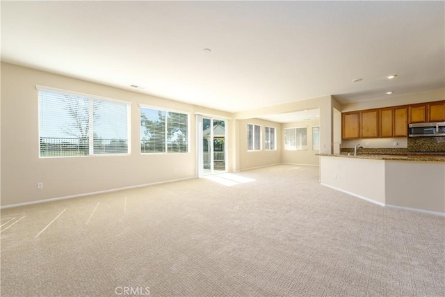 unfurnished living room with light carpet, baseboards, a sink, and recessed lighting