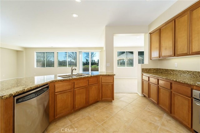 kitchen with appliances with stainless steel finishes, brown cabinetry, a sink, and light stone countertops