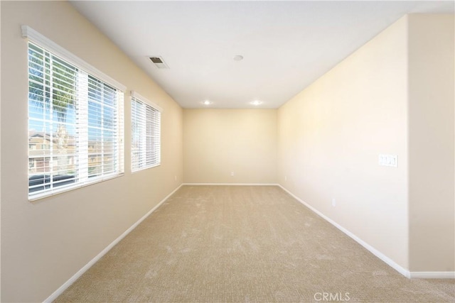 empty room featuring light colored carpet, visible vents, and baseboards