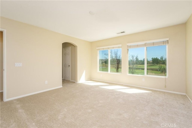 empty room with arched walkways, light carpet, visible vents, and baseboards