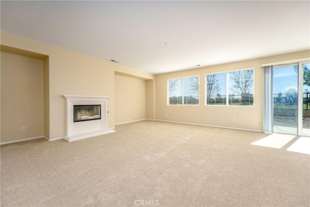 unfurnished living room featuring a glass covered fireplace, light colored carpet, visible vents, and baseboards