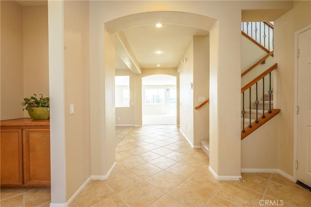 hallway featuring arched walkways, light tile patterned flooring, stairway, and baseboards