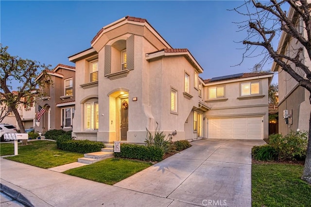 mediterranean / spanish-style home featuring driveway, solar panels, stucco siding, an attached garage, and a front yard