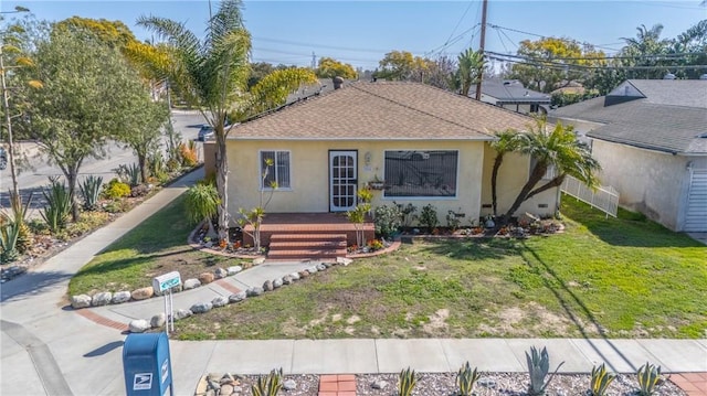 bungalow featuring a shingled roof, a front yard, fence, and stucco siding