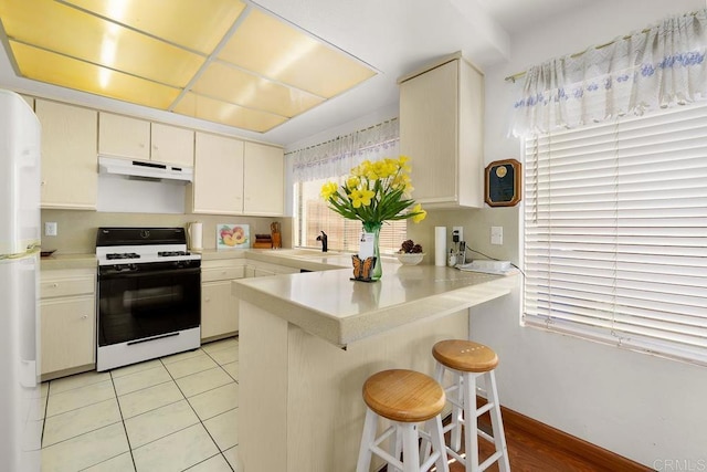 kitchen featuring range with gas stovetop, a breakfast bar, light countertops, a peninsula, and under cabinet range hood