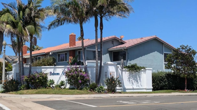 view of front facade with a chimney, a tile roof, and stucco siding