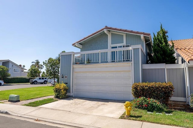 view of front facade featuring a garage, concrete driveway, a balcony, fence, and a front yard