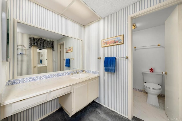 bathroom with a textured ceiling, vanity, toilet, and wallpapered walls