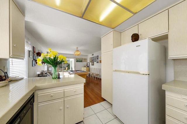 kitchen with cream cabinetry, light tile patterned floors, light countertops, freestanding refrigerator, and dishwasher