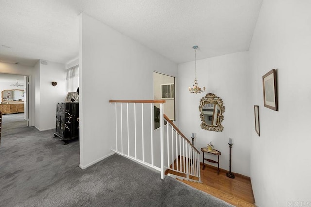 hallway featuring a chandelier, dark colored carpet, and an upstairs landing