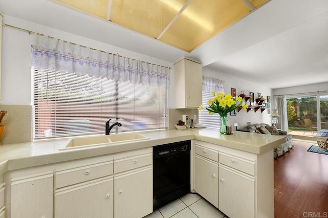 kitchen featuring a peninsula, a sink, black dishwasher, light countertops, and cream cabinetry