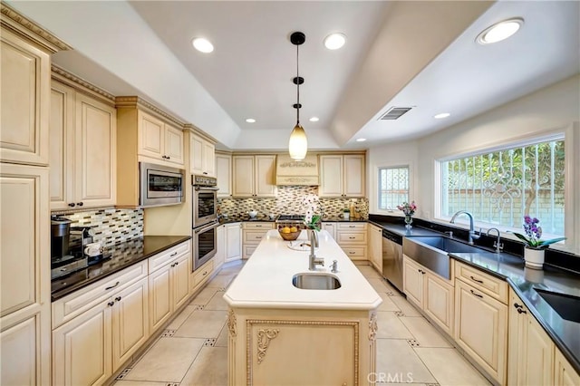 kitchen with cream cabinets, stainless steel appliances, a sink, and a raised ceiling